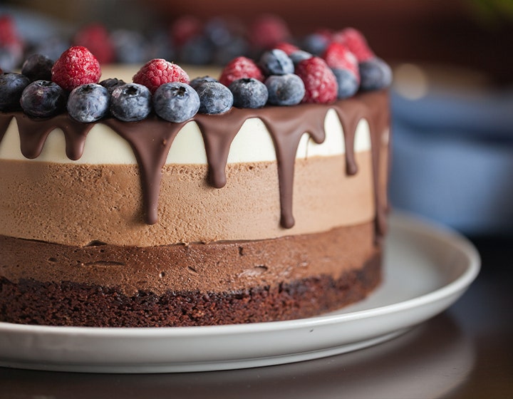 A layered chocolate mousse cake with chocolate drips and topped with fresh berries