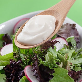 A wooden spoon full of creamy mayonnaise-style dressing over a bowl of salad, highlighting cost-saving egg alternatives